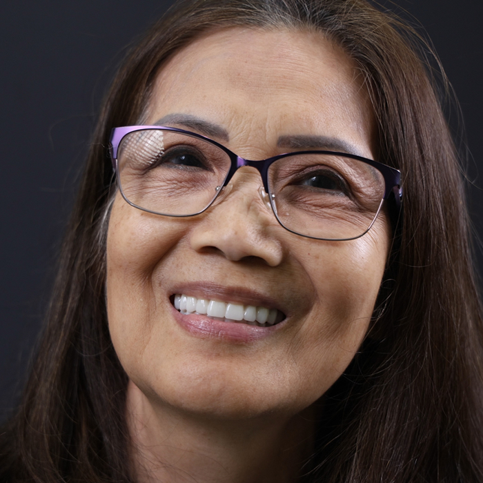 A woman with long brown hair and glasses smiles while looking upwards.