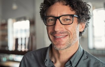 Man with curly hair and glasses smiling indoors.