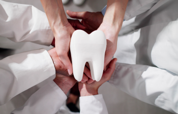 Group of people in white coats holding a large tooth model together, viewed from above.